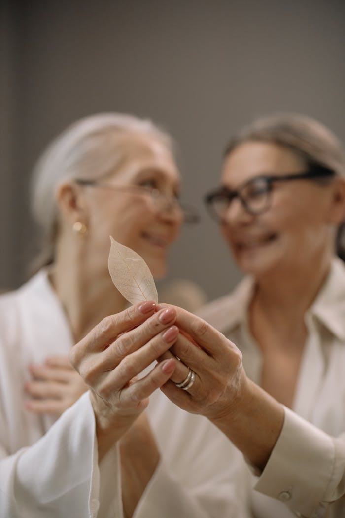 Two senior women smiling while holding an autumn leaf indoors, fostering community and joy.