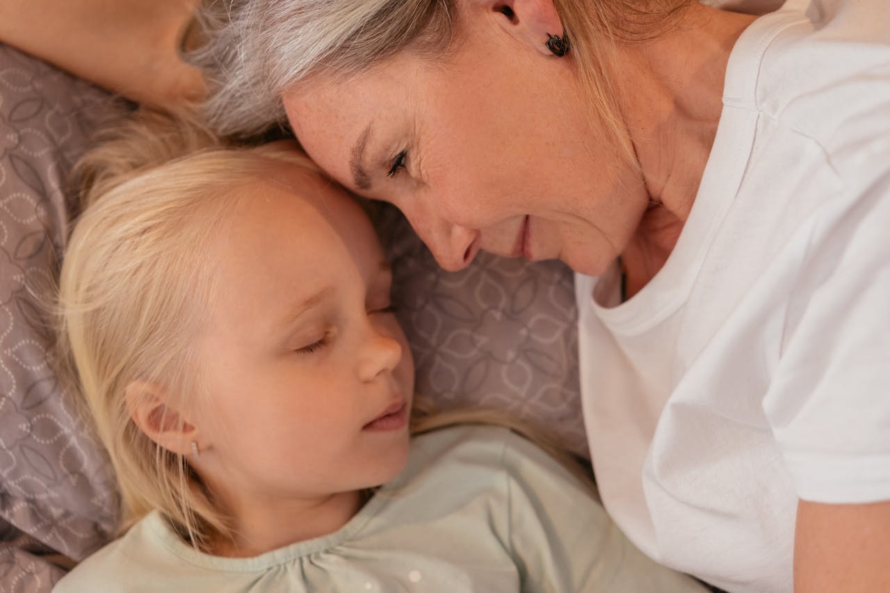Grandmother and granddaughter sharing a tender, loving moment while lying close together indoors.